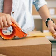 Close-up image of post worker applying adhesive tape on cardboard boxes